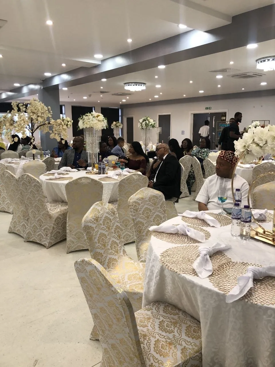 Guests seated at round tables with gold damask chair covers and crystal centrepieces at P2 Centre, Erith