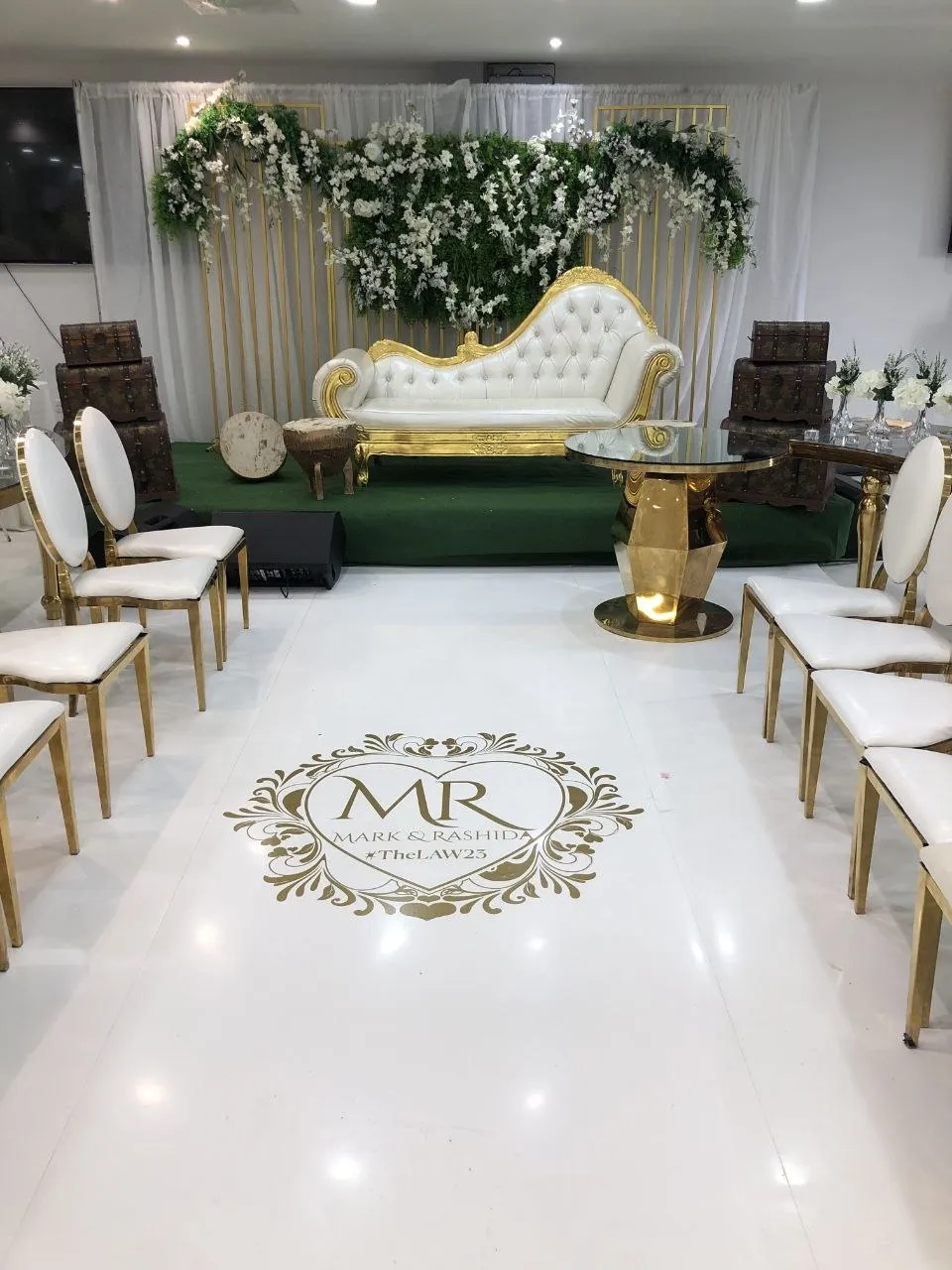 Wedding stage with white and gold chaise, floral wall and monogrammed dance floor at P2 Centre, Erith