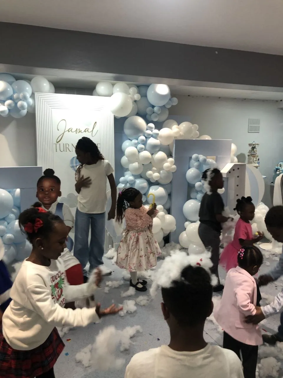 Children playing at a first birthday party with a blue and white balloon backdrop at P2 Centre, Erith