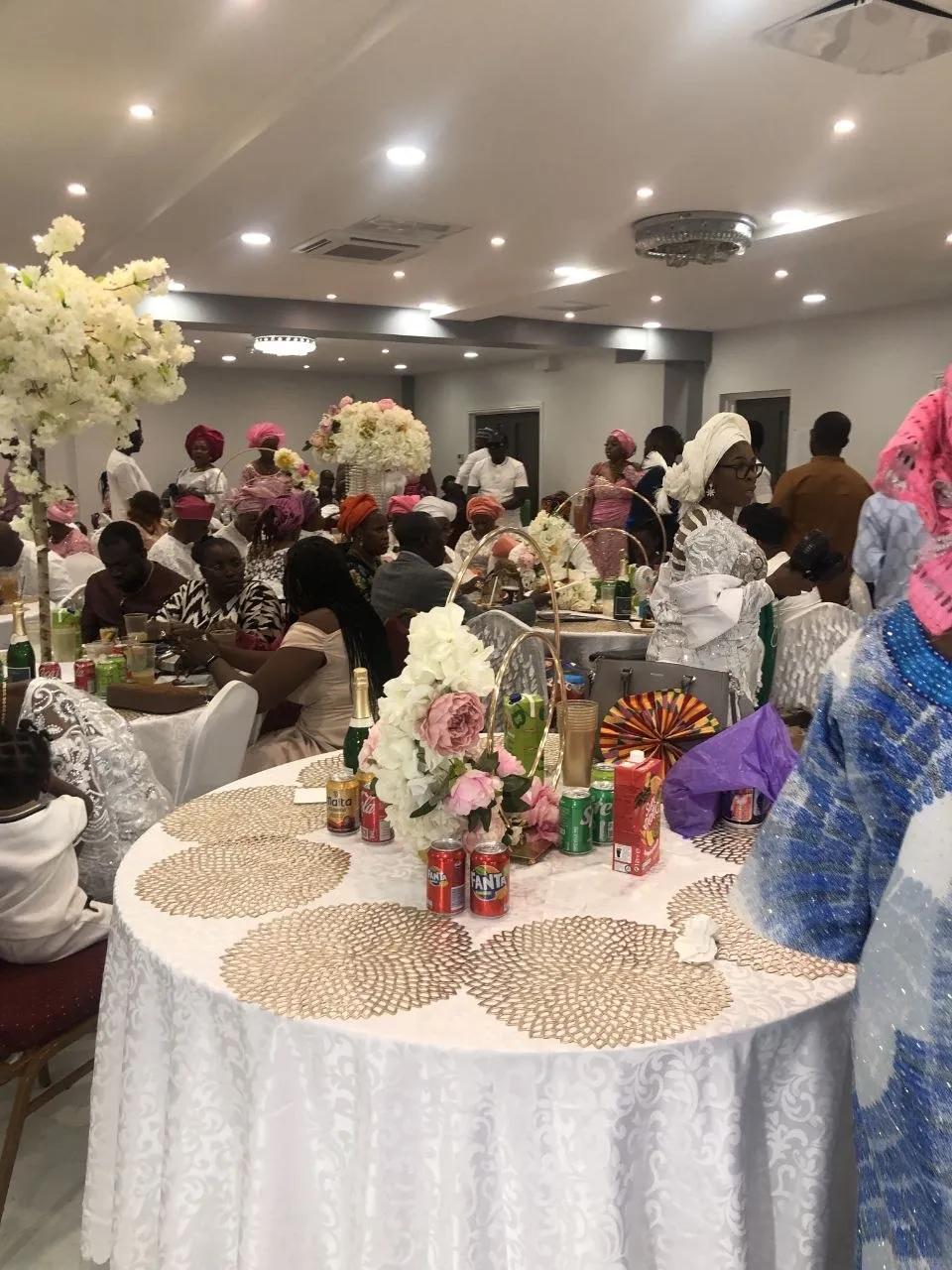 Busy celebration with guests in colourful traditional dress and floral table styling at P2 Centre, Erith