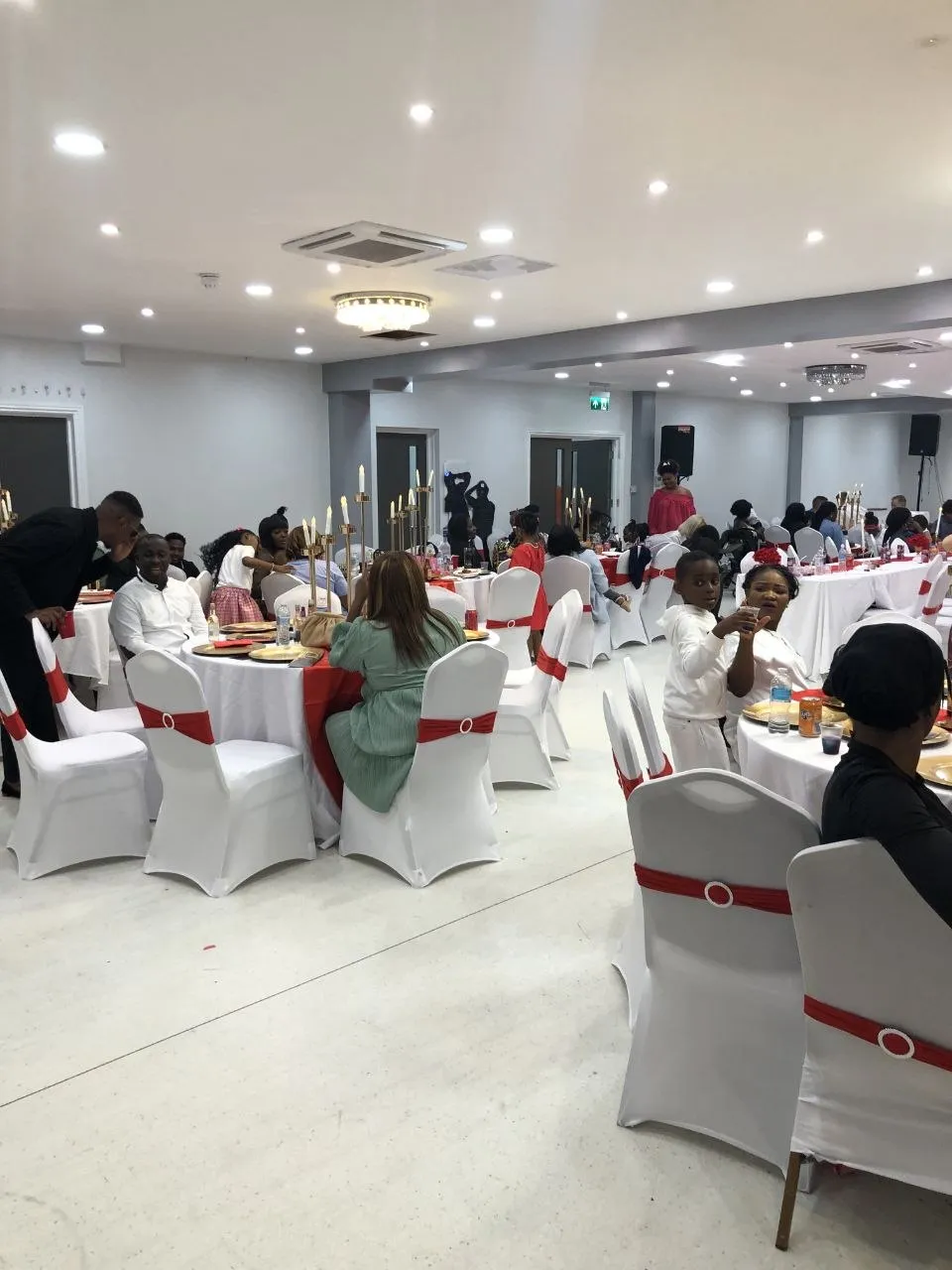 Guests seated at round tables with red sashes during a party at P2 Centre, Erith