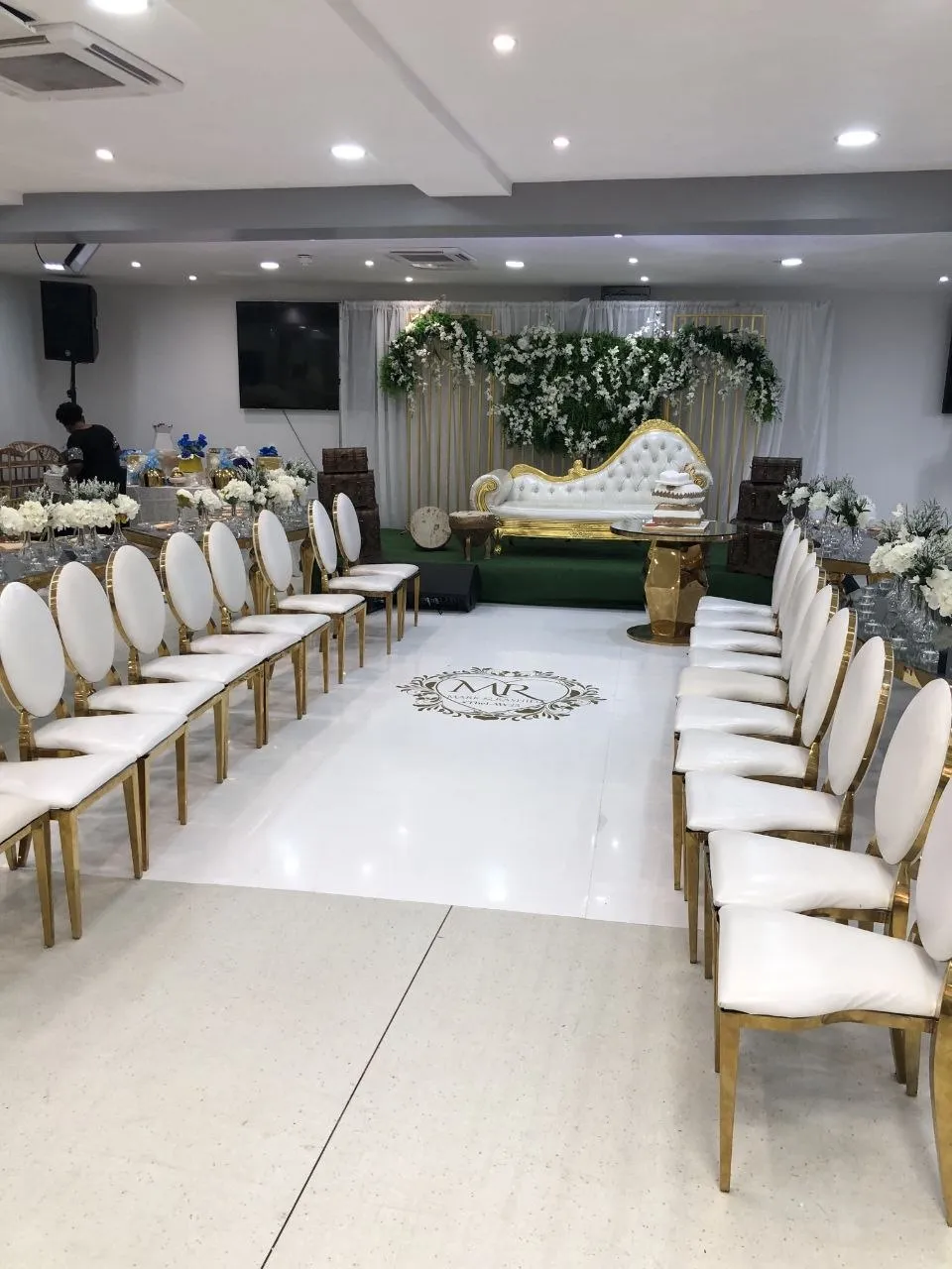 Wedding aisle with white and gold chairs leading to a green and white floral stage at P2 Centre, Erith