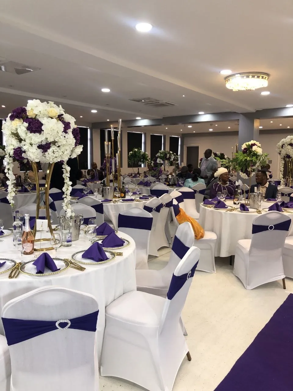 Guests at round tables with purple napkins and tall floral centrepieces at P2 Centre, Erith