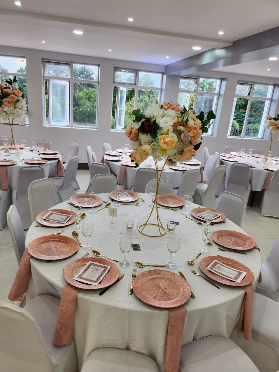 Round banquet table with rose gold chargers and floral centrepiece in the bright P2 Centre hall, Erith