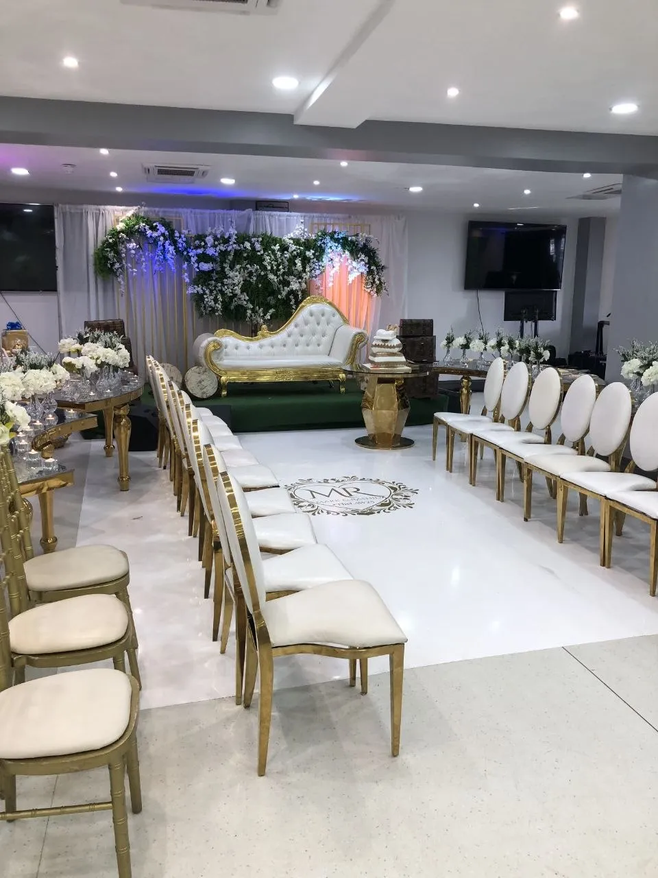 Wedding aisle lined with white and gold chairs leading to the floral stage at P2 Centre, Erith